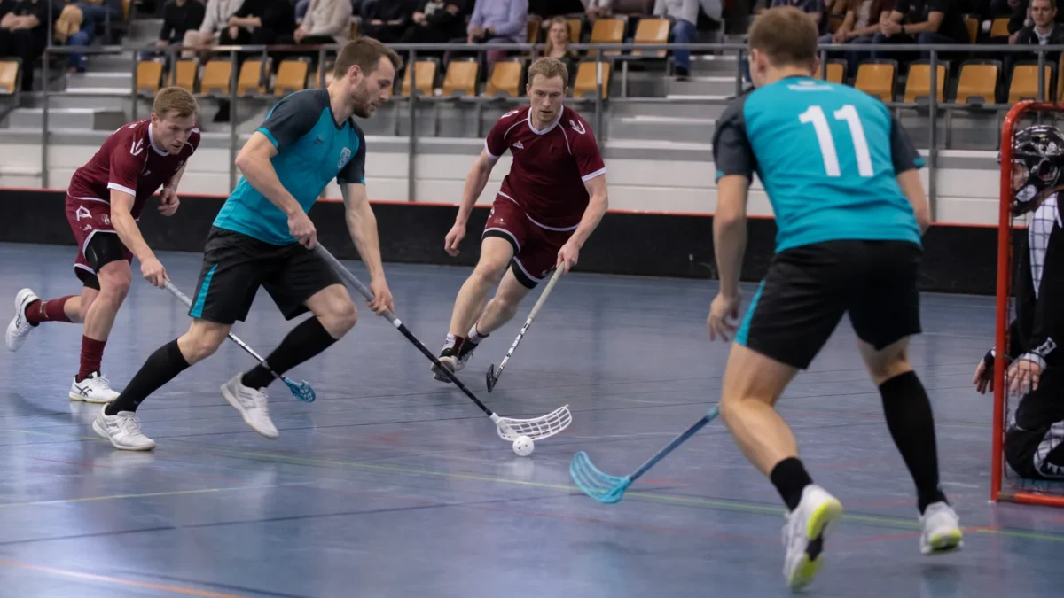Anonyma innebandyspelare med hålboll på ett sportgolv i en inomhushall.